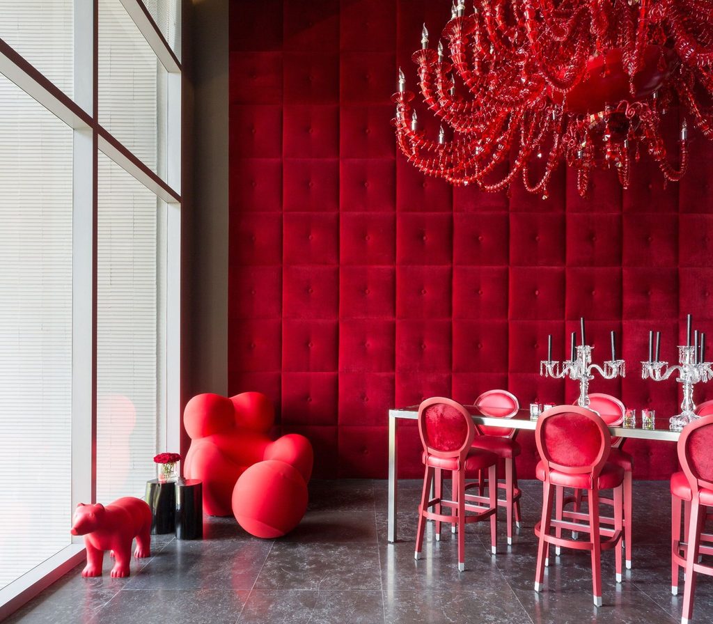 Salón de Yoo Panama con pared de terciopelo rojo capitoné, chandelier rojo y mobiliario Starck