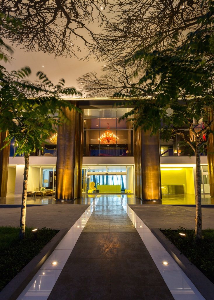 Entrada iluminada de Yoo Panama by Starck al anochecer, con columnas de madera y chandelier visible en el lobby